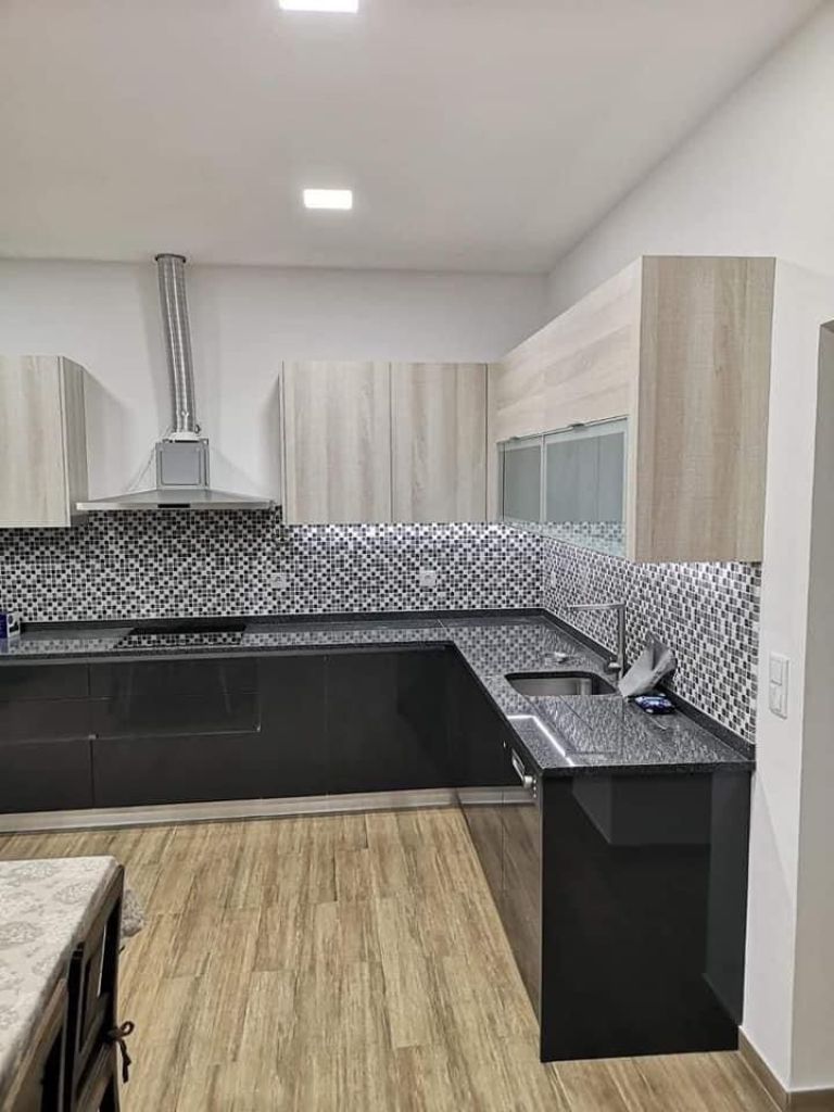 Cozinha em madeira natural com bancada preta e exaustor suspenso